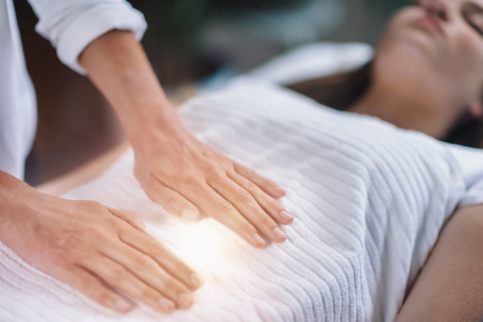 Cropped Hands Of Therapist Giving Reiki Treatment To Teenage Girl On Face At Spa